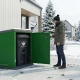 Homeowner accessing ToteBoxx residential bin enclosure in winter, showing easy-open design with black garbage bin inside green steel enclosure in Canadian neighborhood