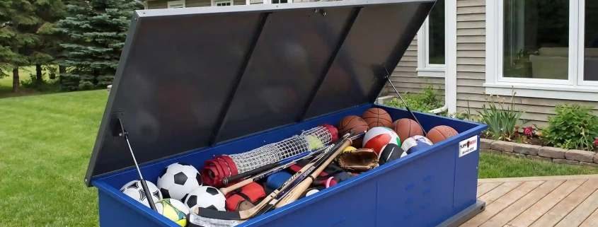 TuffBoxx blue summer storage container on residential deck holding sports equipment including basketballs, soccer balls, baseball bats and gloves demonstrating seasonal storage organization